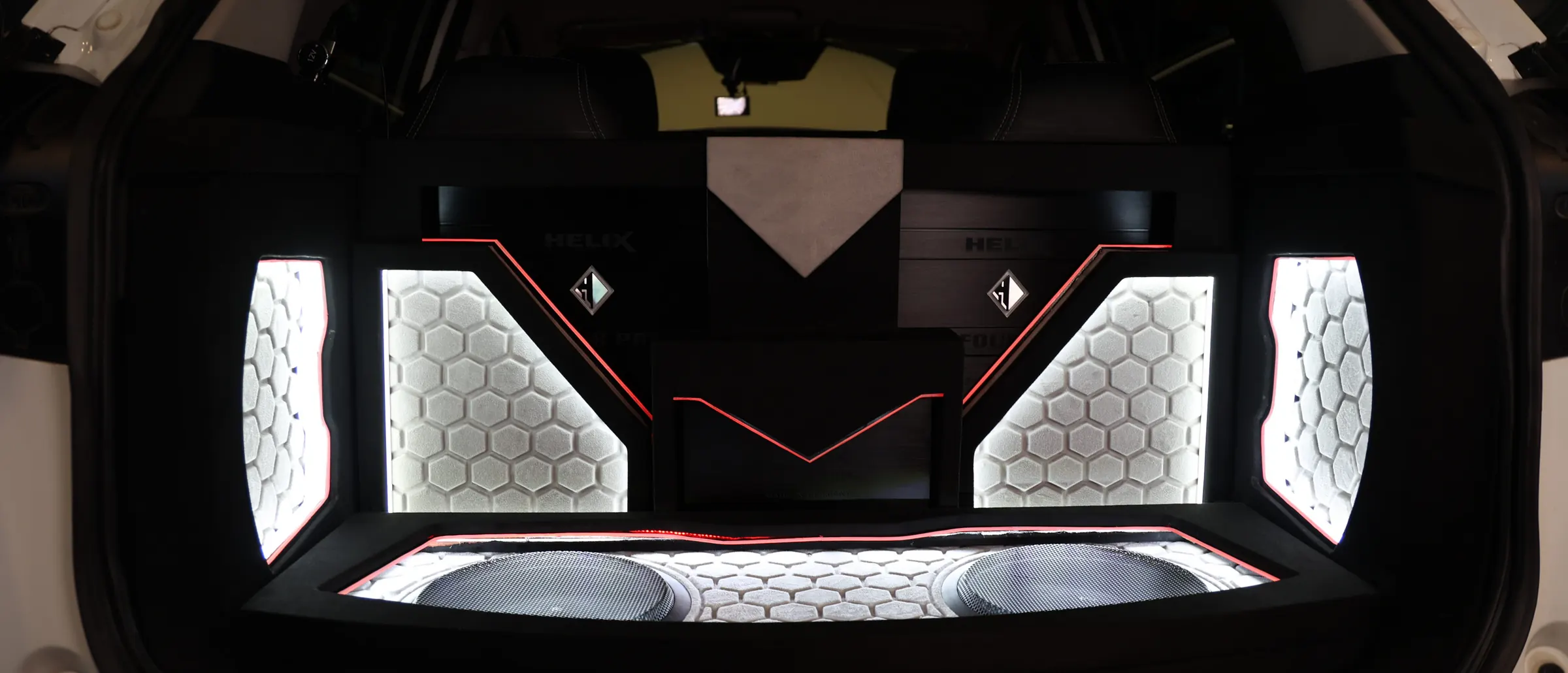 A finished boot: a fabricated hexagon-panel amplifier rack picked out in LED, amplifiers and subwoofer set symmetrically either side