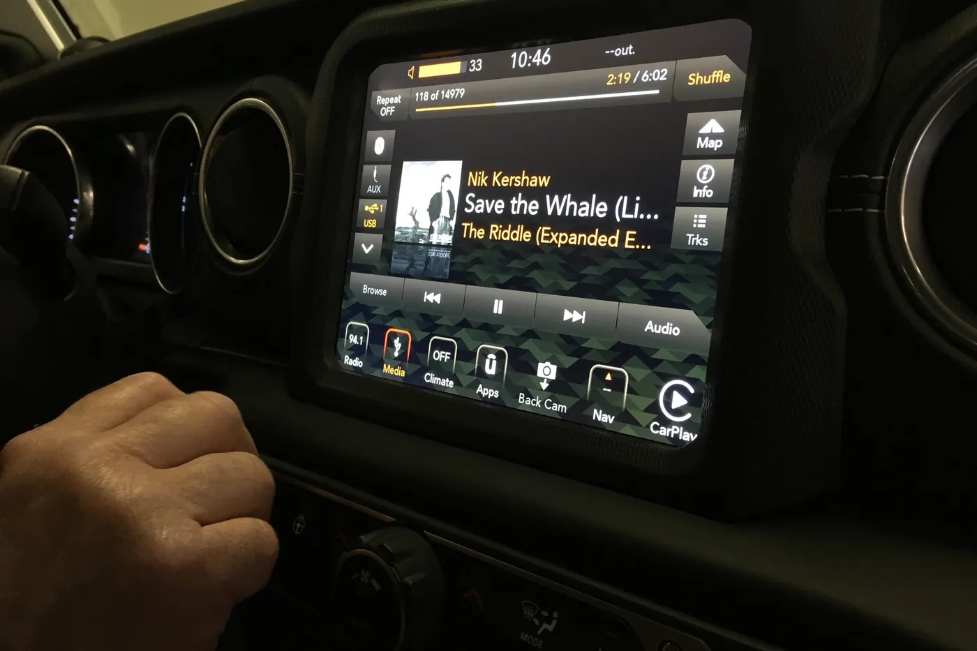 A factory infotainment screen playing music in a Jeep Wrangler dashboard