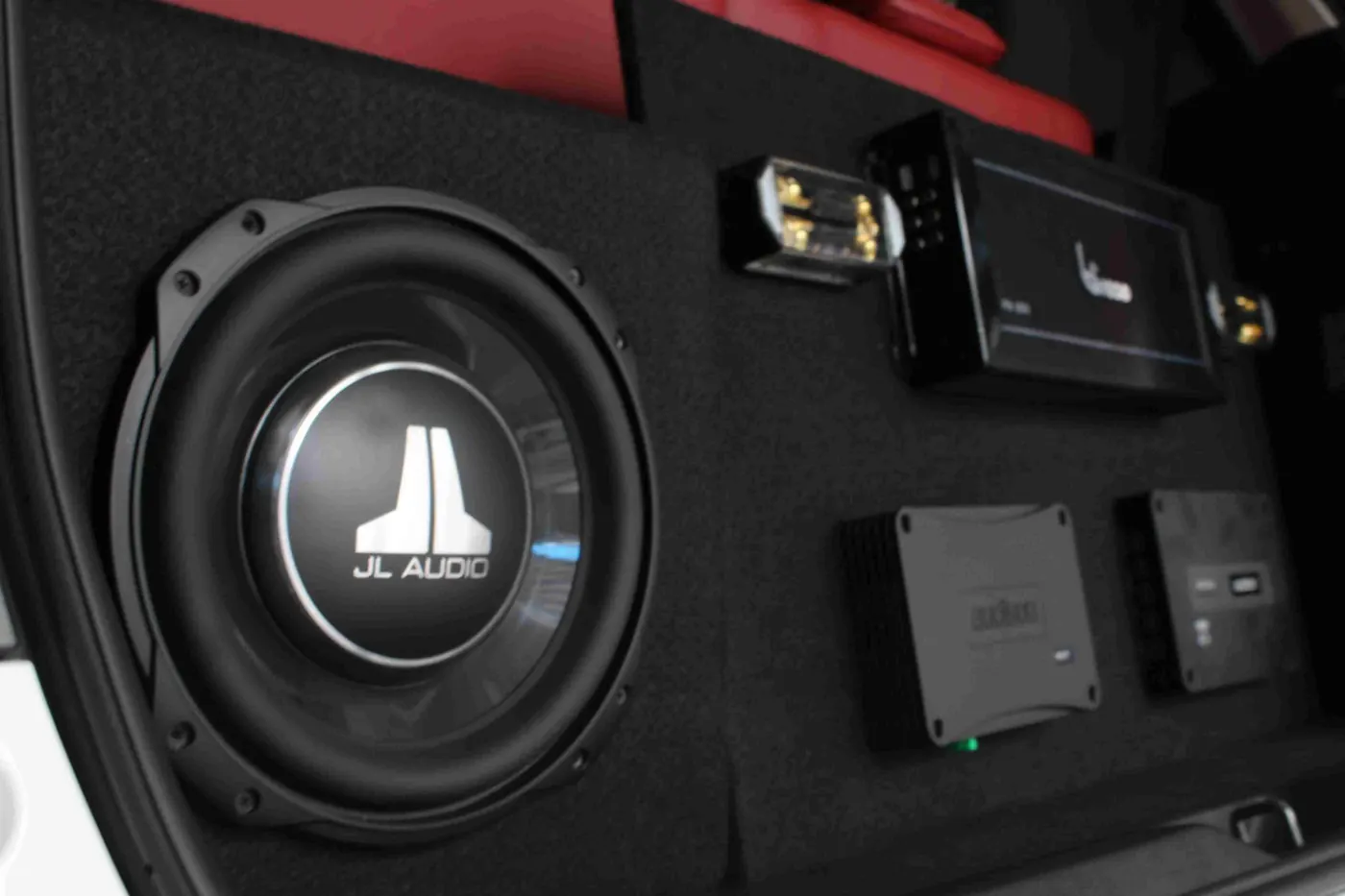 A JL Audio subwoofer and matched amplifiers set into a black-carpet boot panel, red interior trim behind