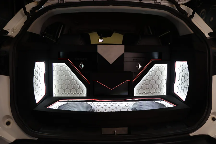 The boot of a white SUV, fabricated symmetrically: backlit hexagon-pattern panels either side, red accent lines, two Helix amplifiers on the rear panel and twin subwoofers behind a hexagon grille.