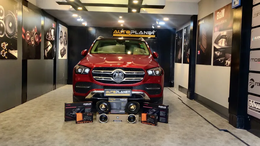 The Auto Planet showroom corridor: a red Mercedes GLE under the Auto Planet sign, brand wall panels down both sides, and Helix and Match component boxes with drivers laid out on the floor in front of the car.