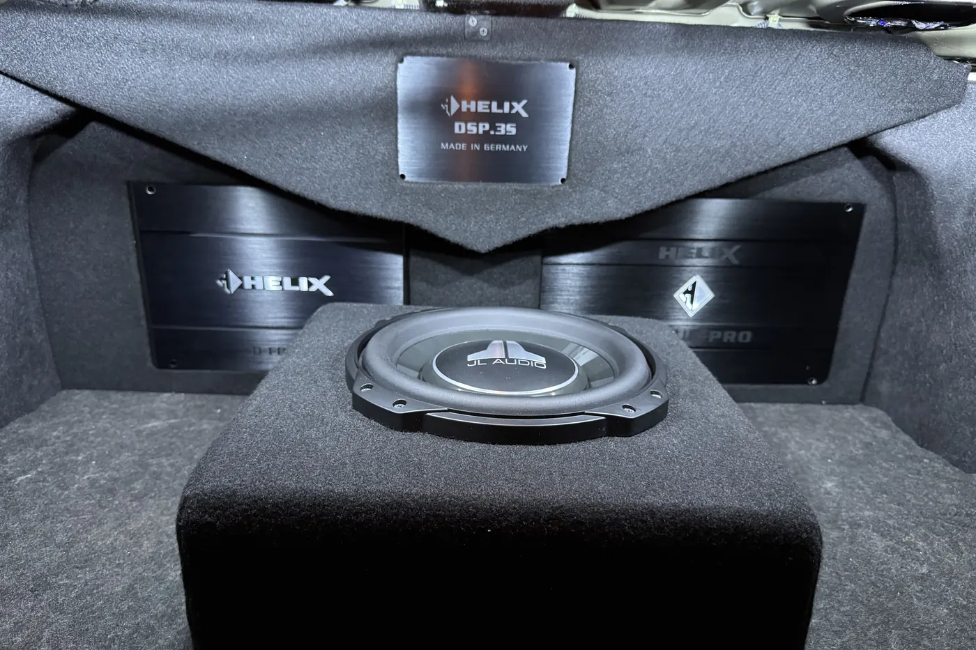 A finished boot build: a JL Audio subwoofer set into black carpet beneath a Helix DSP.3S processor and matched amplifiers