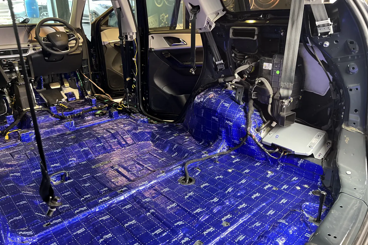 A car stripped to bare metal in the bay, damping laid across the whole floor, both doors open